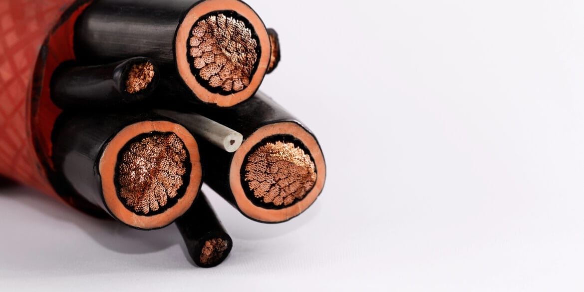 Close-up image of the cross-section of a thick cable showing several bundles of copper wires and one smaller white wire encased in a black and orange outer layer. Close-up image of the cross-section of a thick cable showing several bundles of copper wires and one smaller white wire encased in a black and orange outer layer.