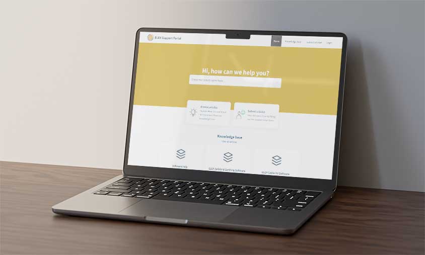 A laptop on a wooden surface displaying a website homepage with a yellow header and search bar.